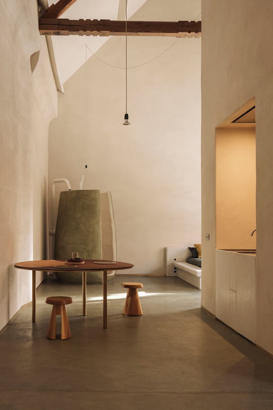 A softly plastered interior with exposed timber beams and minimal pendant lights