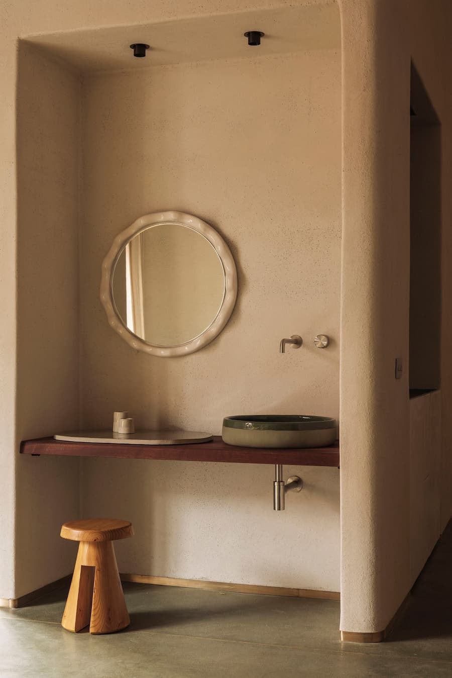 A handcrafted ceramic basin beneath an irregular round mirror set into a textured plaster alcove