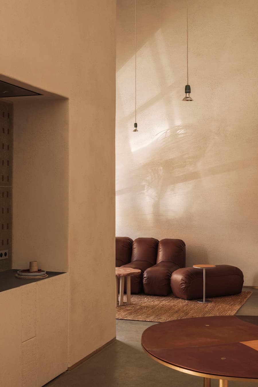 Warm sunlight falls across a textured plaster wall above brown leather lounge seating