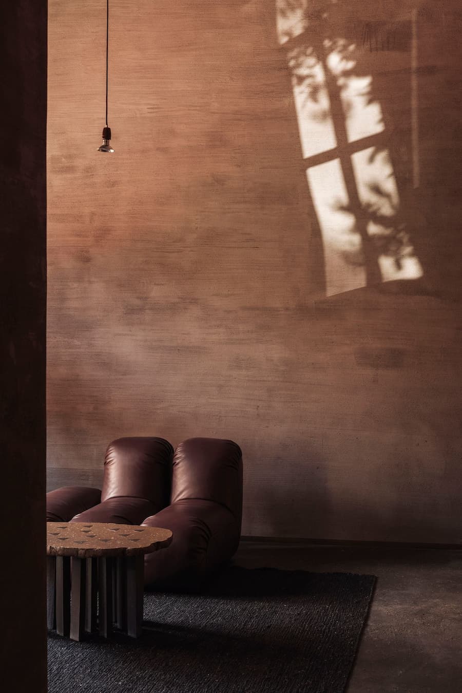 Strong afternoon light casts window shadows across a warm raw-plaster wall beside a leather lounge