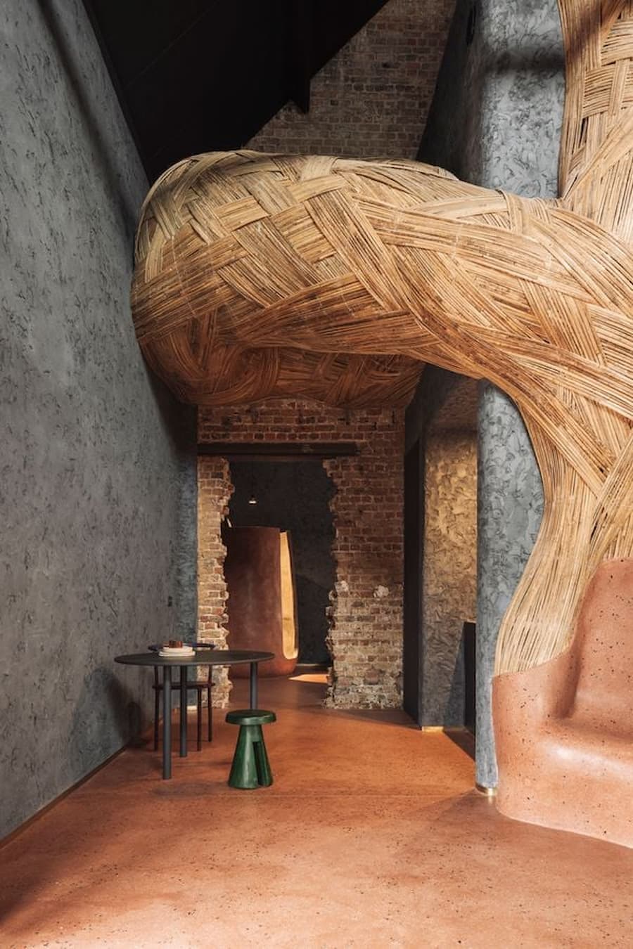 A woven reed structure sweeps around a sculptural terracotta lounge chair inside the historic interior