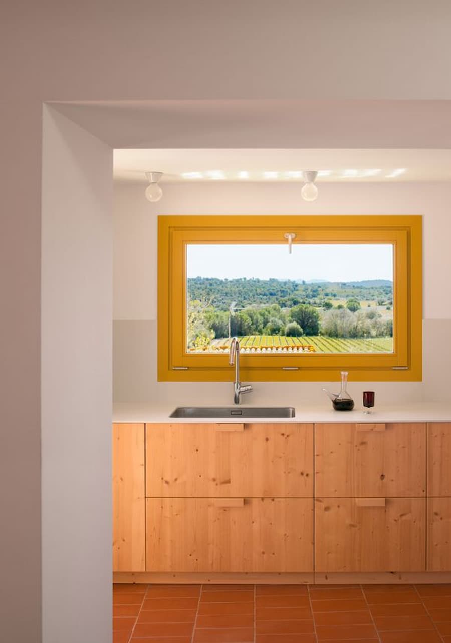 Kitchen framed by a yellow window overlooking the rural landscape at Ca la Carolina.