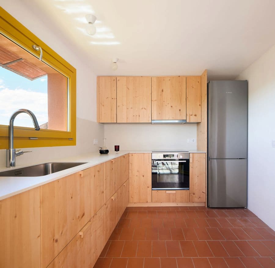 Custom pinewood kitchen with terracotta flooring at Ca la Carolina by Lacol and Altura Arquitectes.