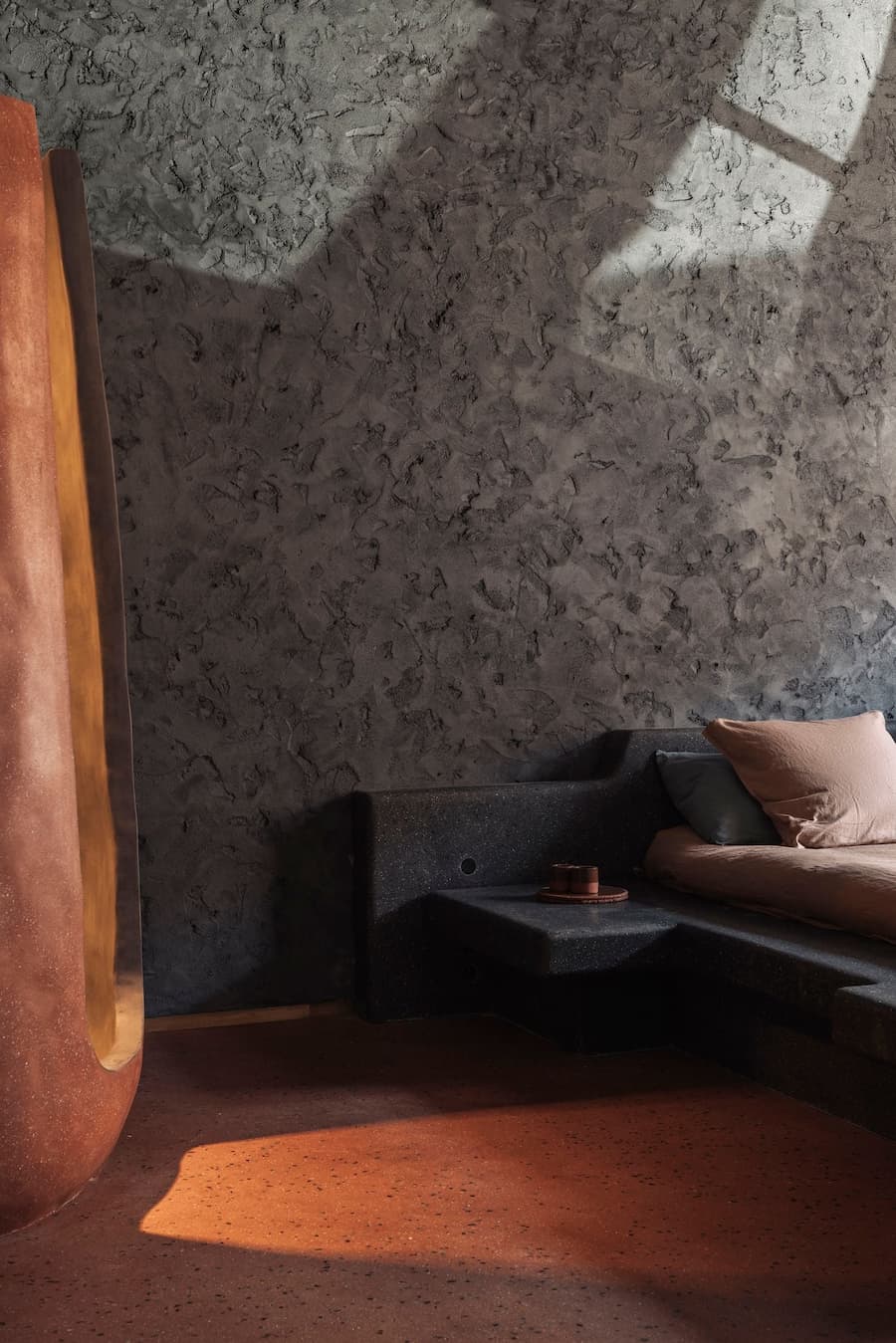 Warm terracotta flooring meets a dark built-in seating platform beneath a textured plaster wall