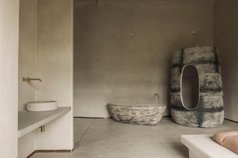 A calm stone-toned bathroom pairs a sculptural freestanding tub with a tall textured bathing structure