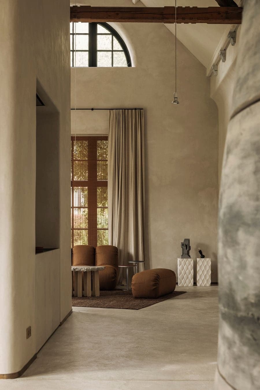 An arched window and timber-framed opening bring filtered daylight into a warm-toned lounge