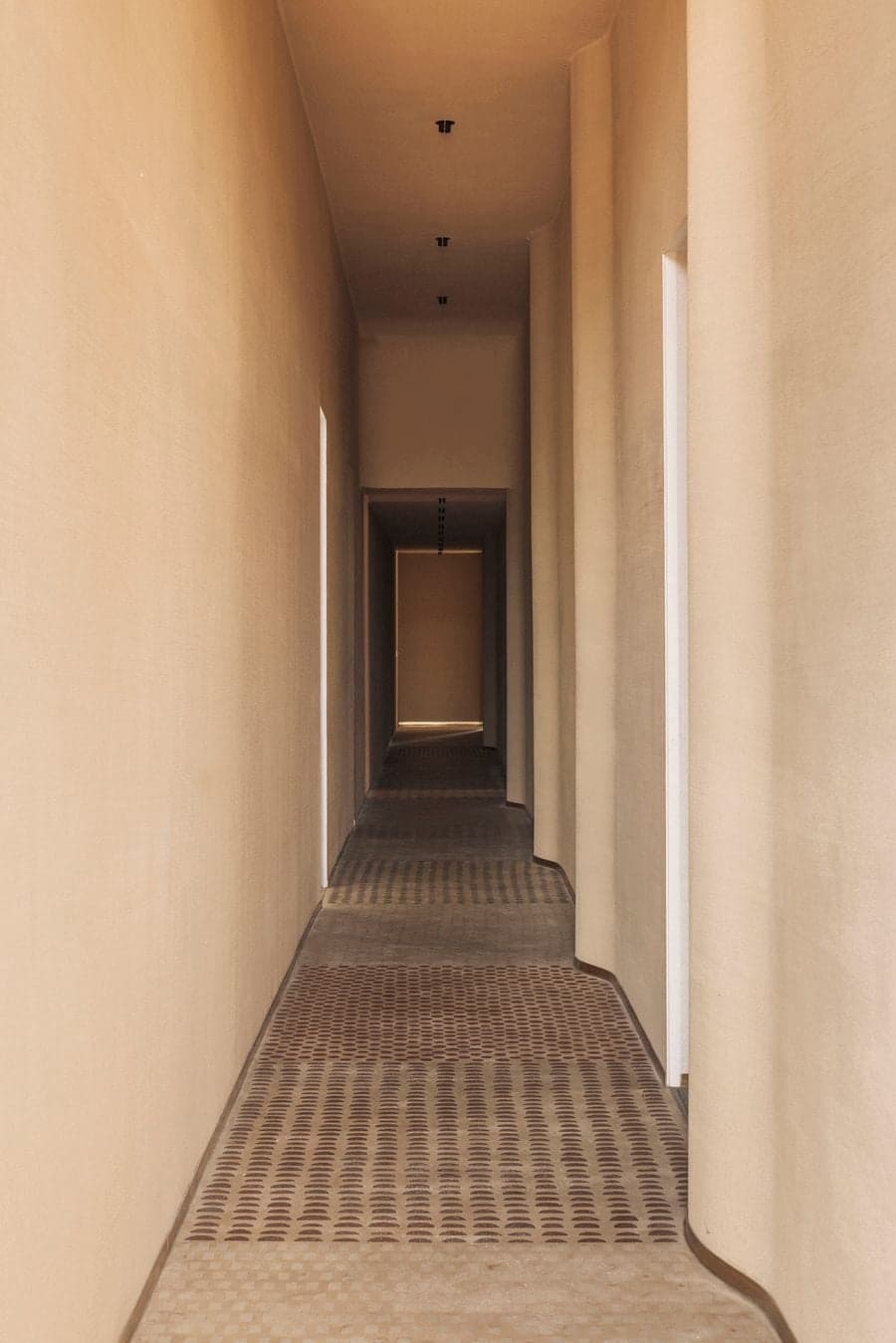 A narrow textured-plaster corridor extends through a sequence of softly lit doorways and patterned flooring