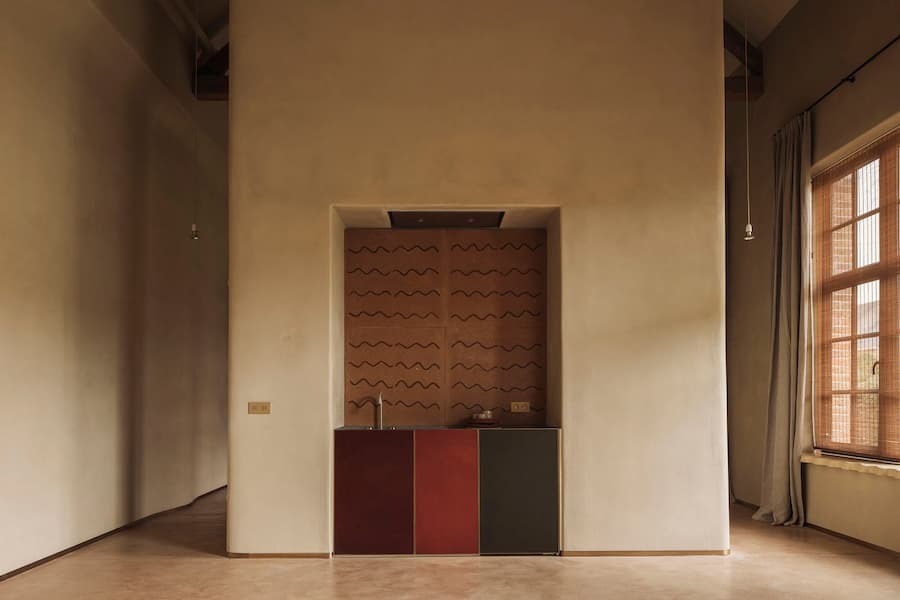 A compact kitchen is recessed into a plaster wall with rust-toned cabinetry and a timber-framed window