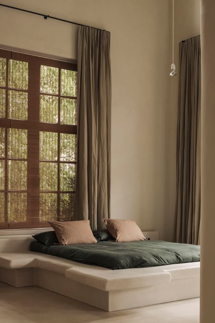 A minimal bedroom combines a low sculptural bed, timber-framed window and full-length linen curtains