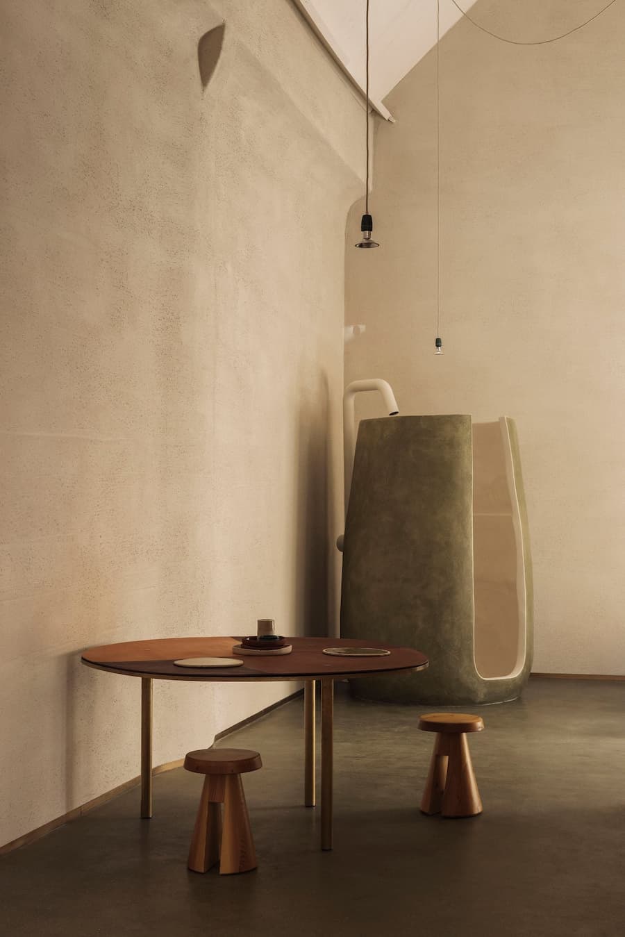 A sculptural bathroom form stands against a softly textured plaster wall beneath suspended pendant lights