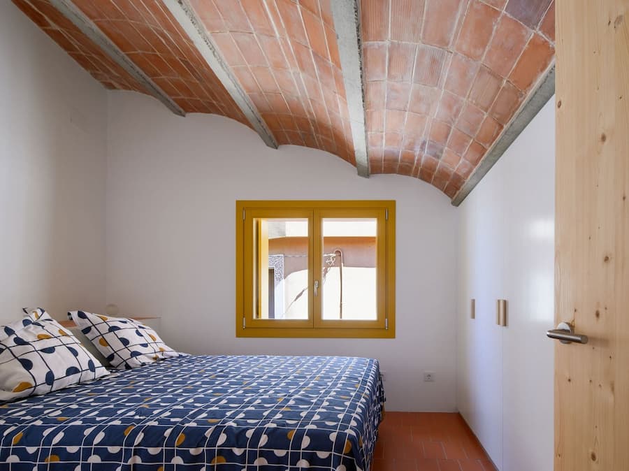 Bedroom beneath the original Catalan vaulted ceiling with a yellow-framed window at Ca la Carolina.