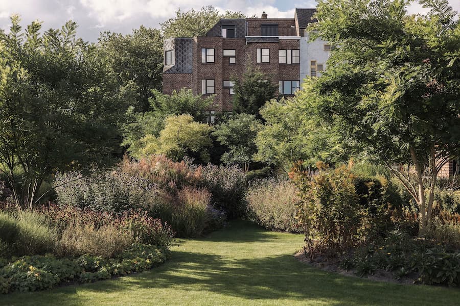 Dense perennial planting frames a brick residential building at the edge of a lush garden
