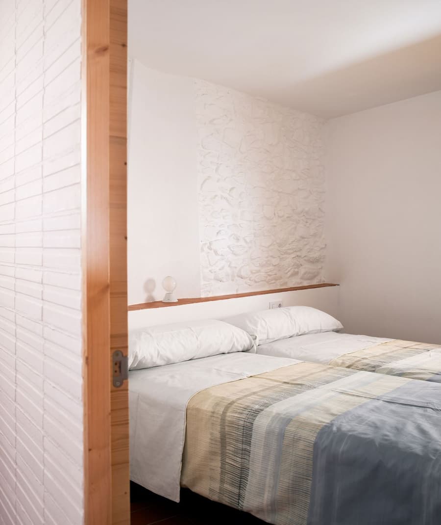 Guest bedroom featuring restored stone wall and soft natural light at Ca la Carolina.