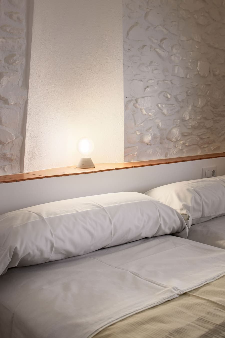 Bedroom with restored stone wall integrated into the headboard niche at Ca la Carolina.