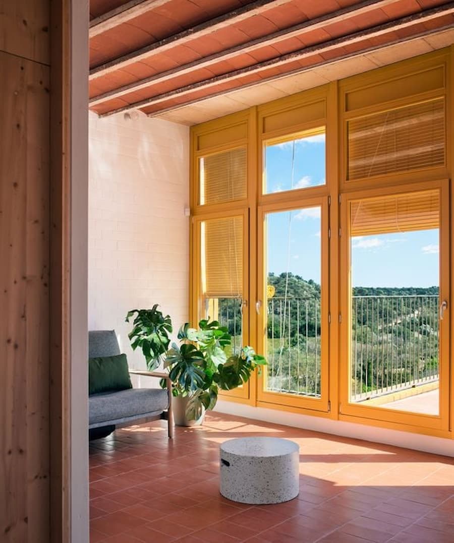 Living area with yellow-framed windows opening toward the rural landscape at Ca la Carolina.