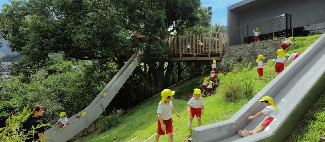 children playing on grassy hillside slides integrated with architecture and natural landscape to reimagine childhood play experiences